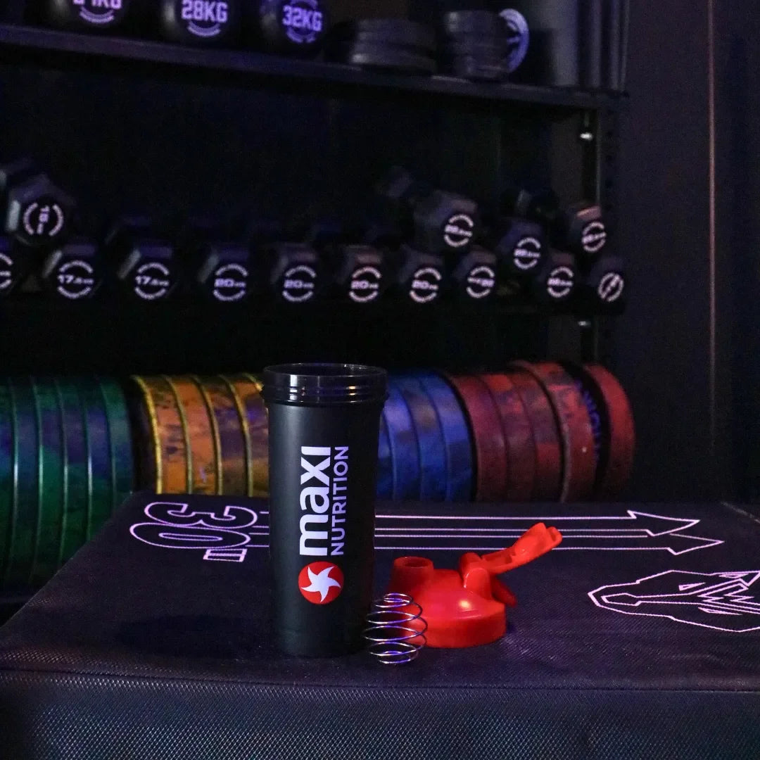 Maxi Nutrition tumbler on a gym mat with weightlifting equipment in the background