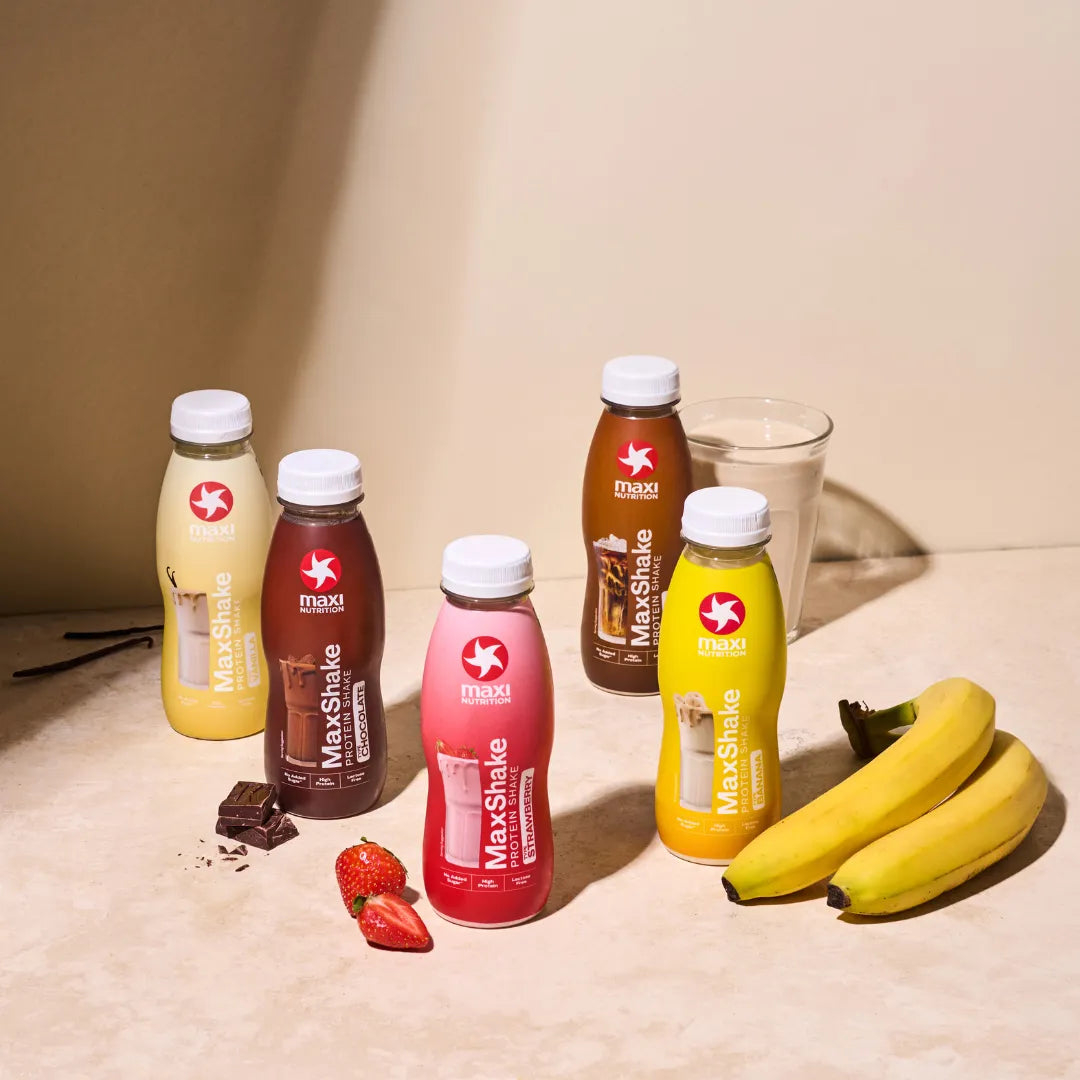 Maxi Shake bottles in various flavors with bananas on a beige surface